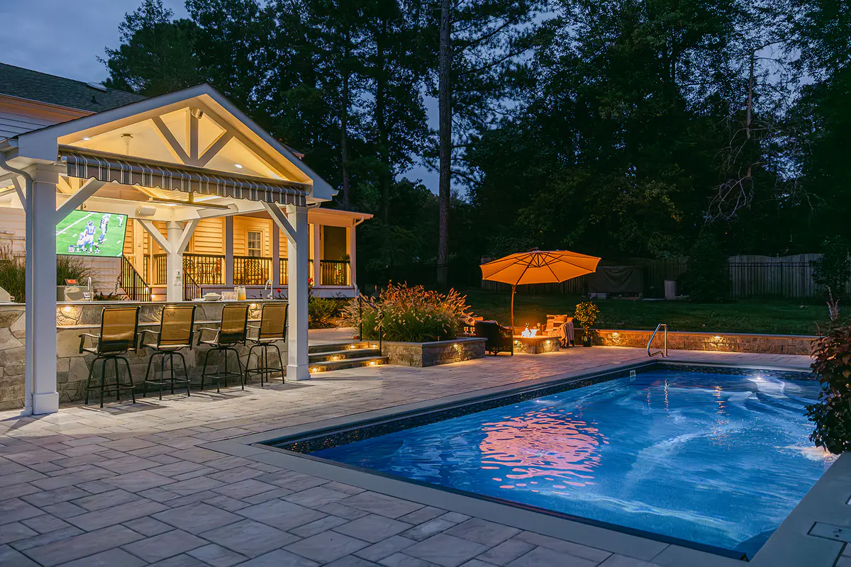 pool in backyard at night with pavilion and tv in the background