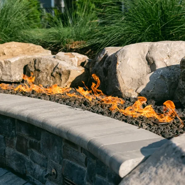 Stone fire feature glowing beside fiberglass pool