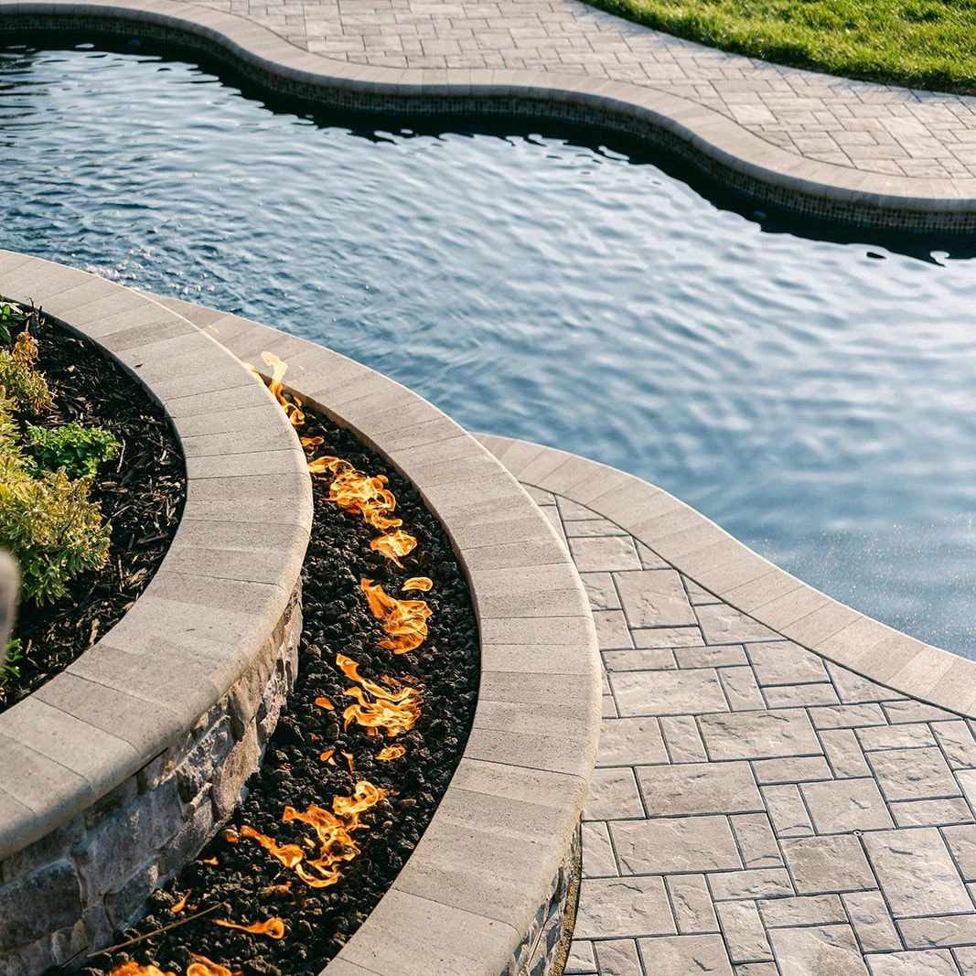 Stone fire feature glowing beside fiberglass pool 