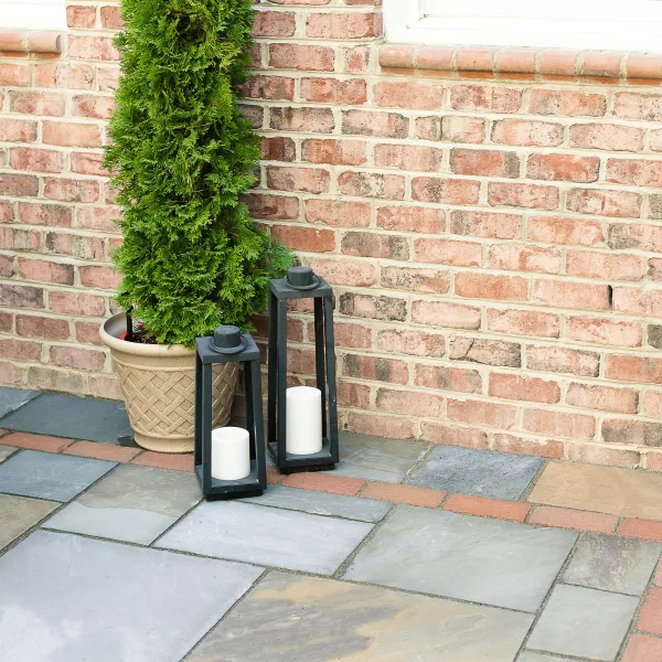 Two large outdoor candles placed beside a tall fern on the back patio