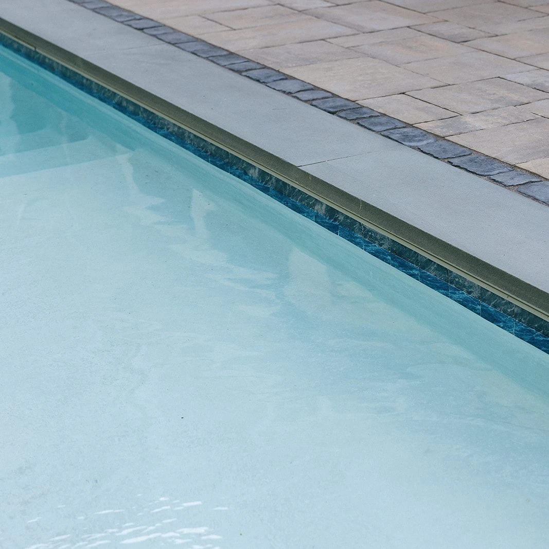 Elegant stone pool deck with thermaled bluestone coping and warm grey tones
