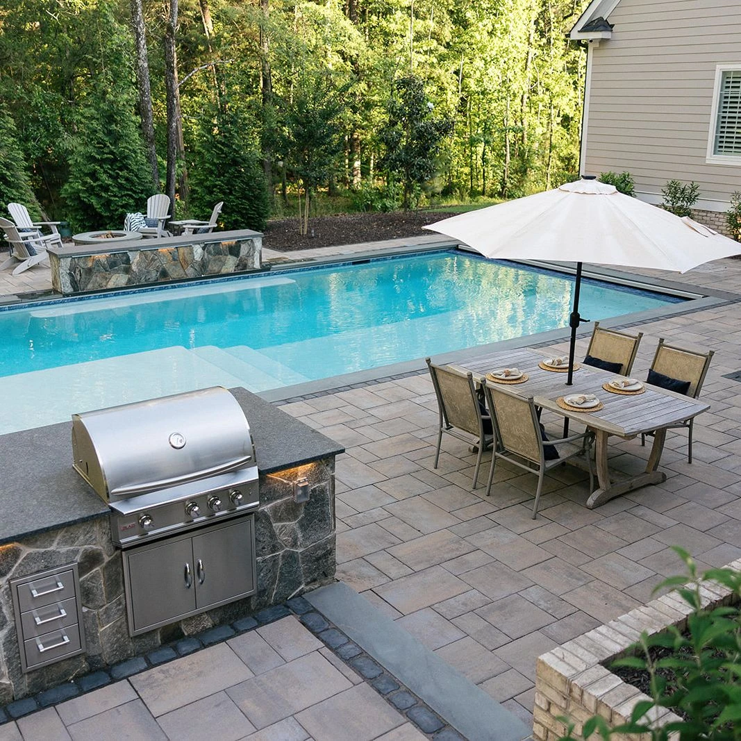 Modern pool area with outdoor kitchen, layered hardscape, and lighting