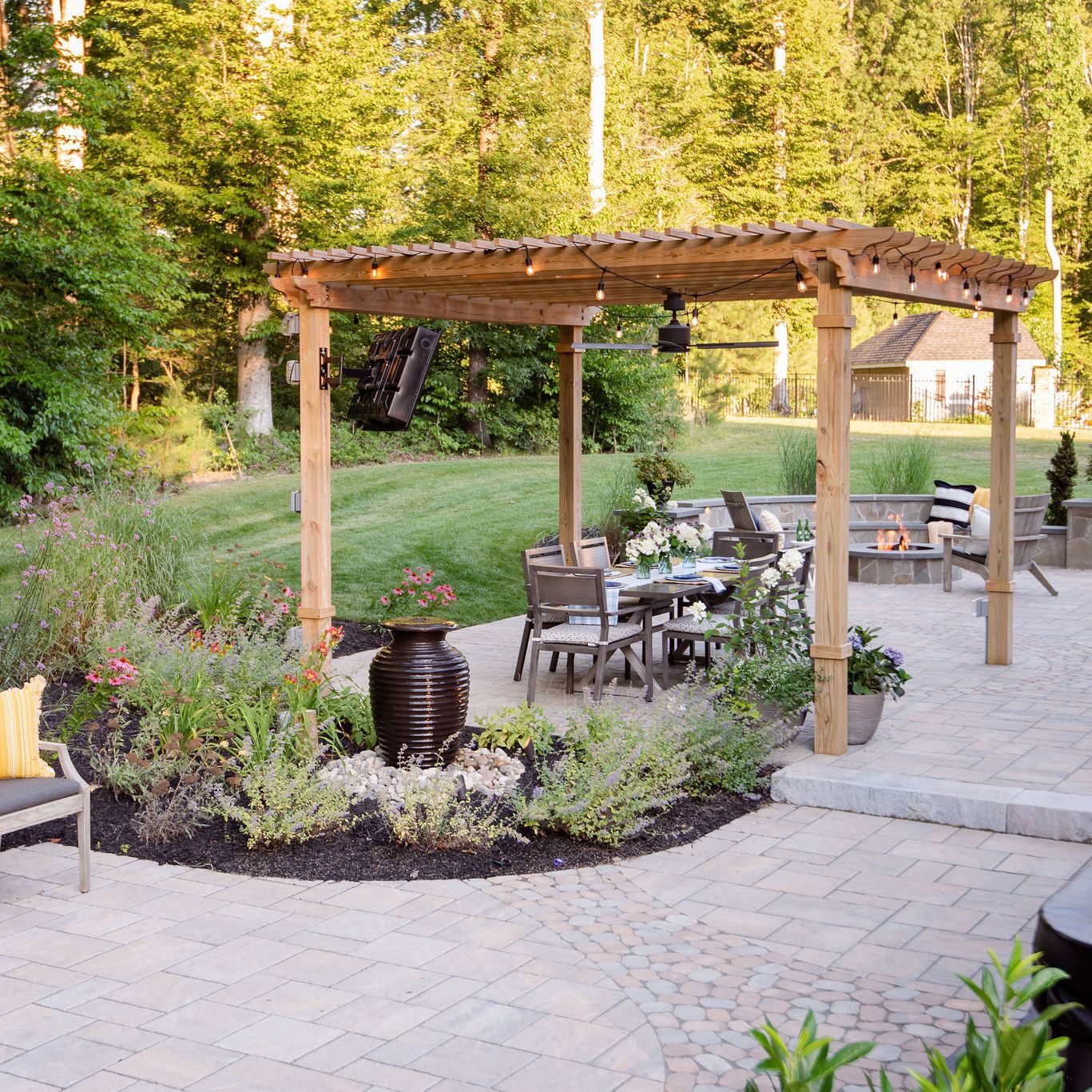 Expansive paver patio with landscaping, bubbling urn, pergola, hot tub, and fire pit.