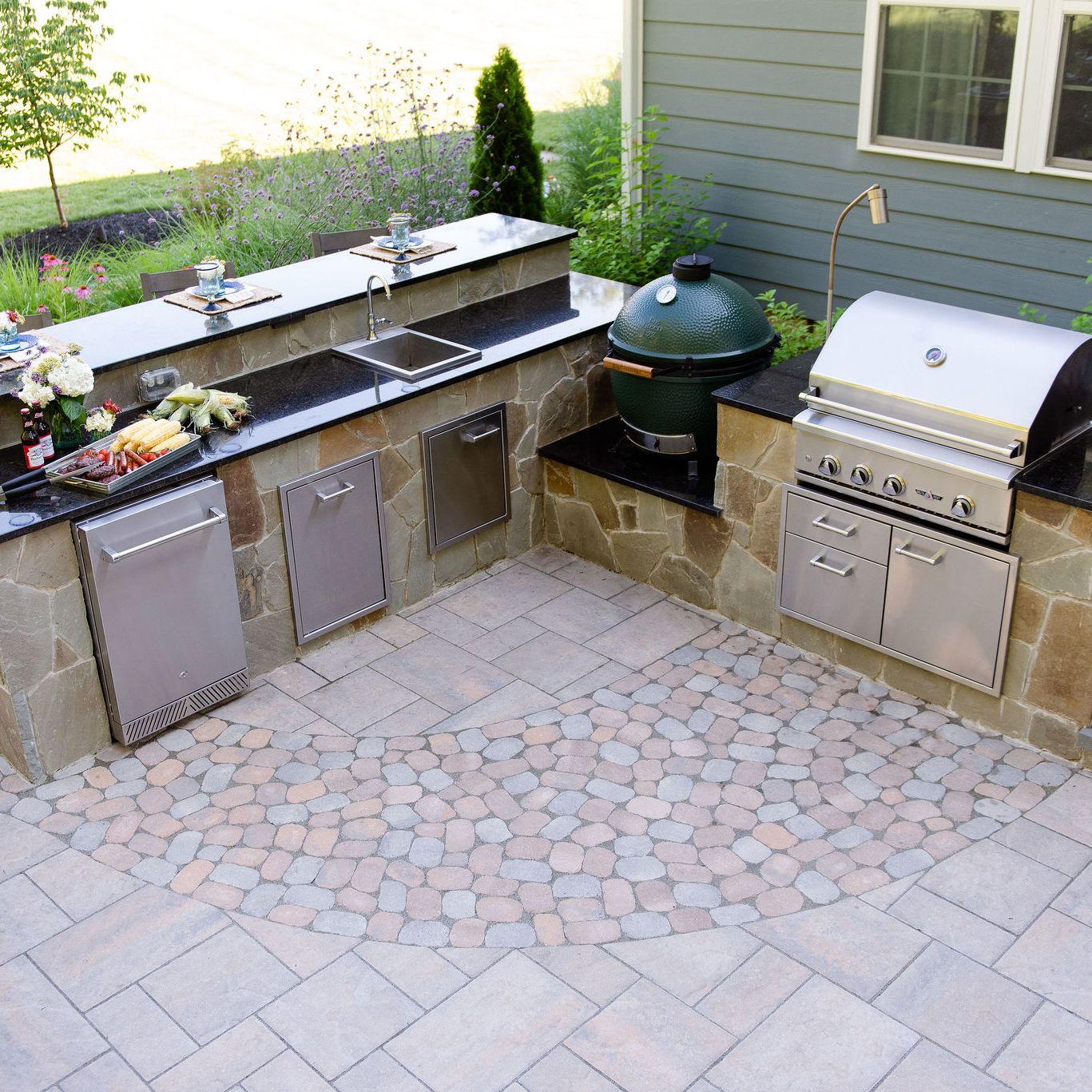 Outdoor kitchen with grill, big green egg smoker, sink, refrigerator and bar top seating