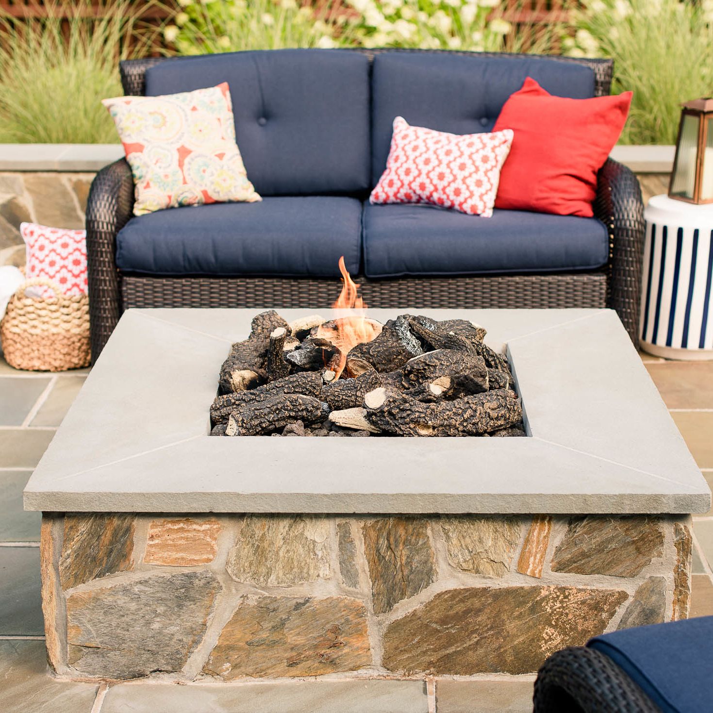 Stone veneer gas fire pit and wicker loveseat with navy blue cushions