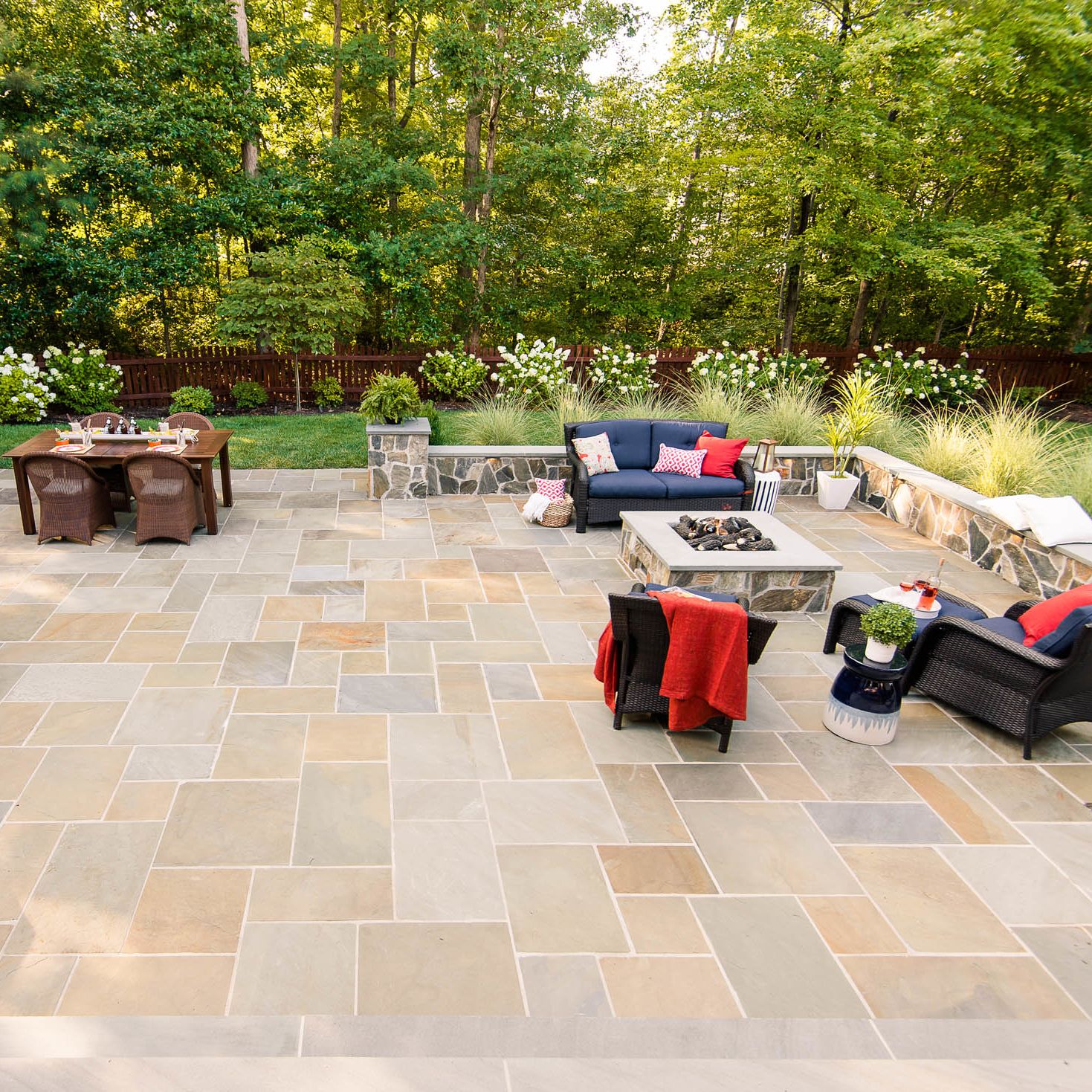 spacious backyard stone paver patiosurrounded with sitting walls and furnished with couches and a fire pit