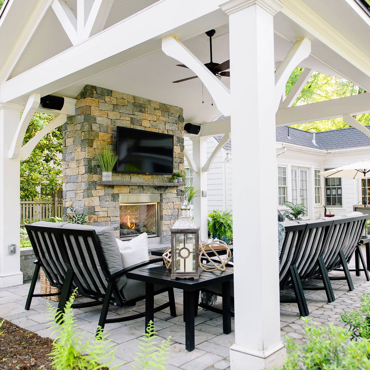 Fully furnished back patio with fireplace and TV under white pavilion