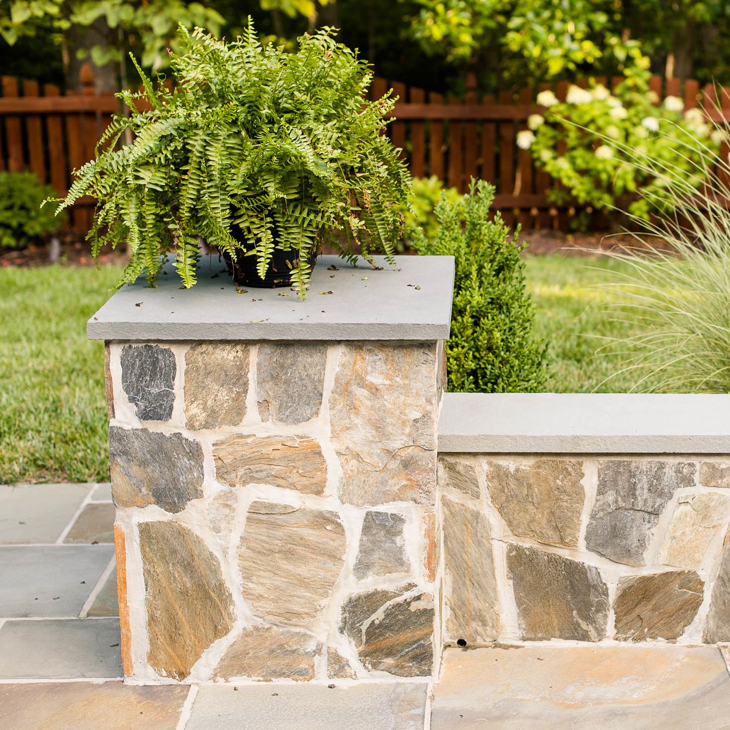 Stone veneer sitting wall with short pillar and green fern sitting on top